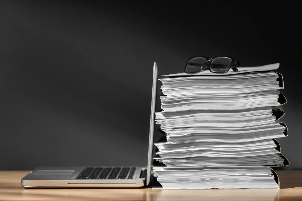 Stack of documents beside laptop